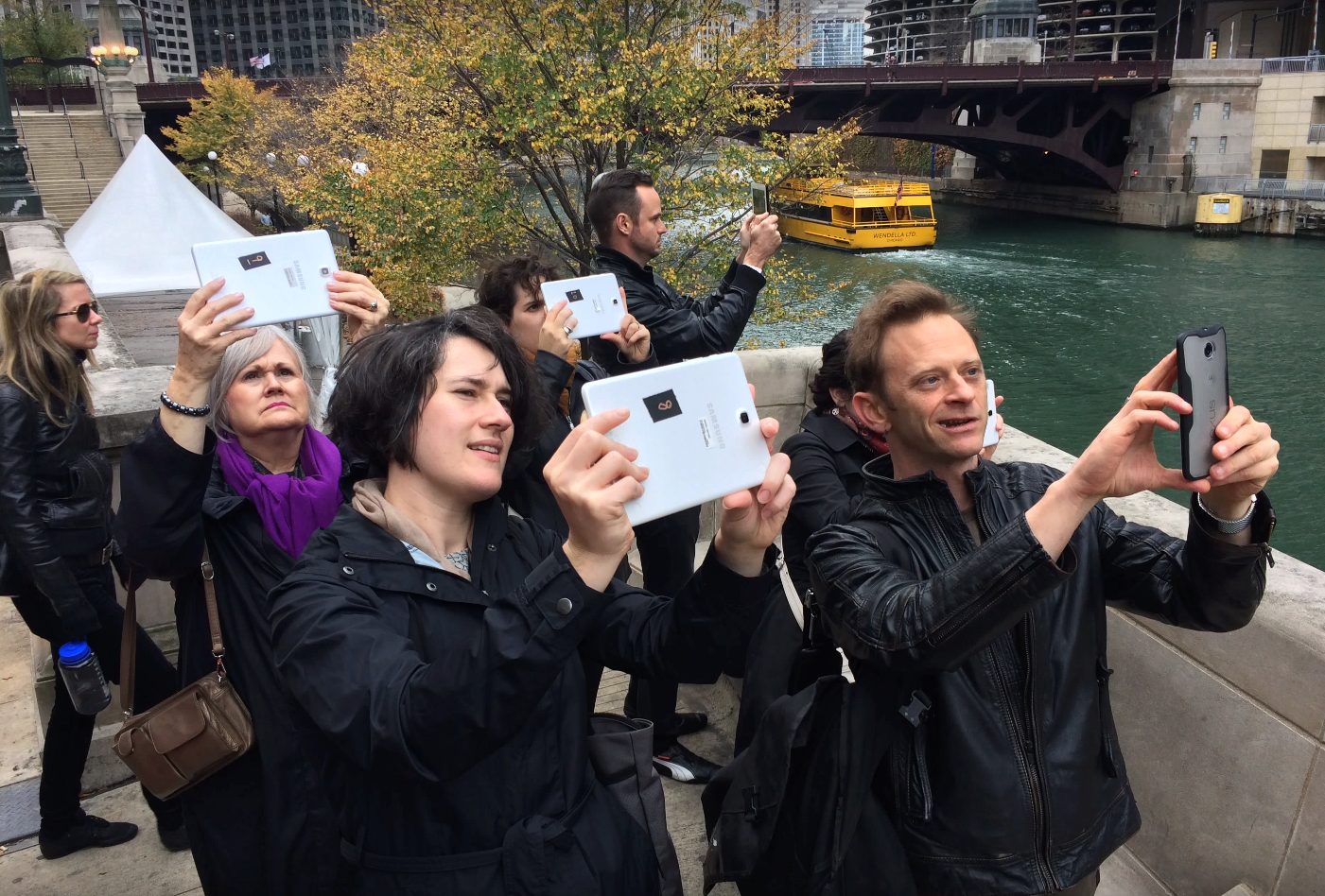A group of people testing the <i>Riverwalk</i> AR application with both smartphone and tablet devices along the Chicago River.