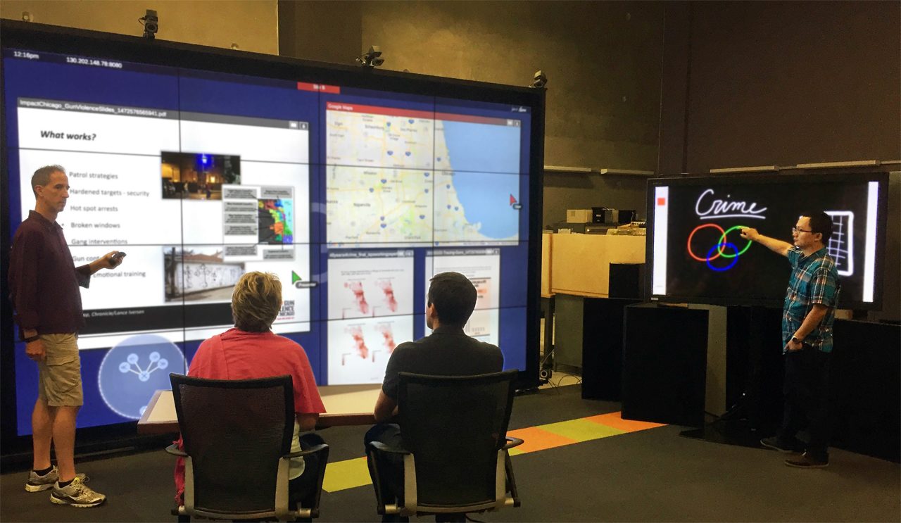 Collaborators gather in front of a large-scale display to share research findings and utilize a multitouch digital whiteboard to brainstorm next steps to advance their work.